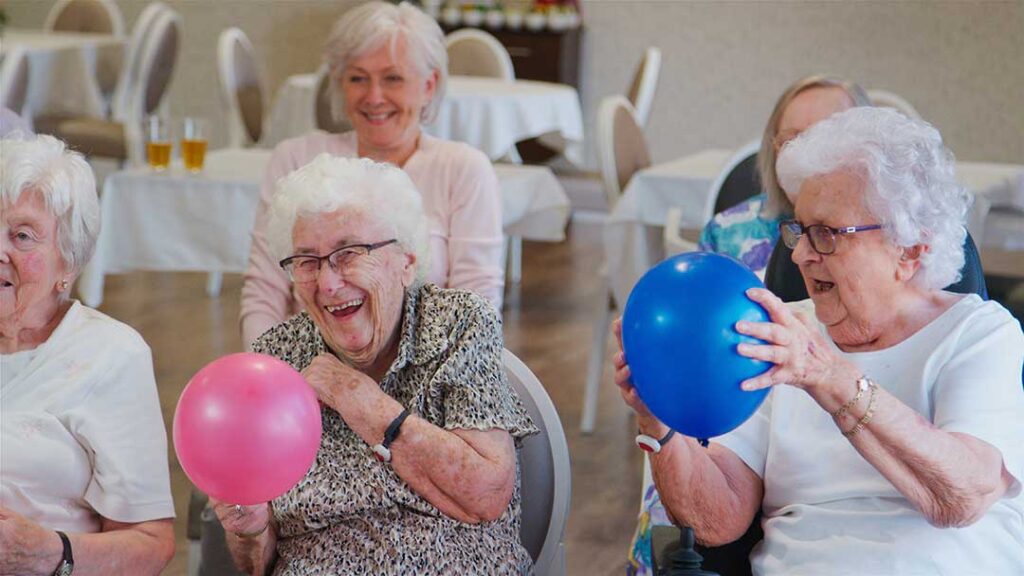Care facility staff assisting older adults during a fire drill evacuation with visible exit signs and safety vests.