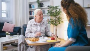 Older couple sits together in an accessible apartment while a caregiver reviews a daily care plan.