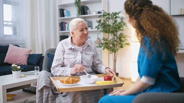 Older couple sits together in an accessible apartment while a caregiver reviews a daily care plan.