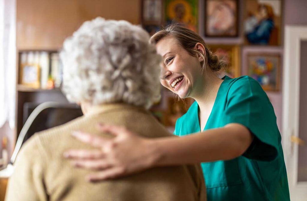 Smiling older adults sitting in a well-lit common living area with a staff member assisting nearby