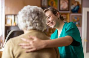 Smiling older adults sitting in a well-lit common living area with a staff member assisting nearby